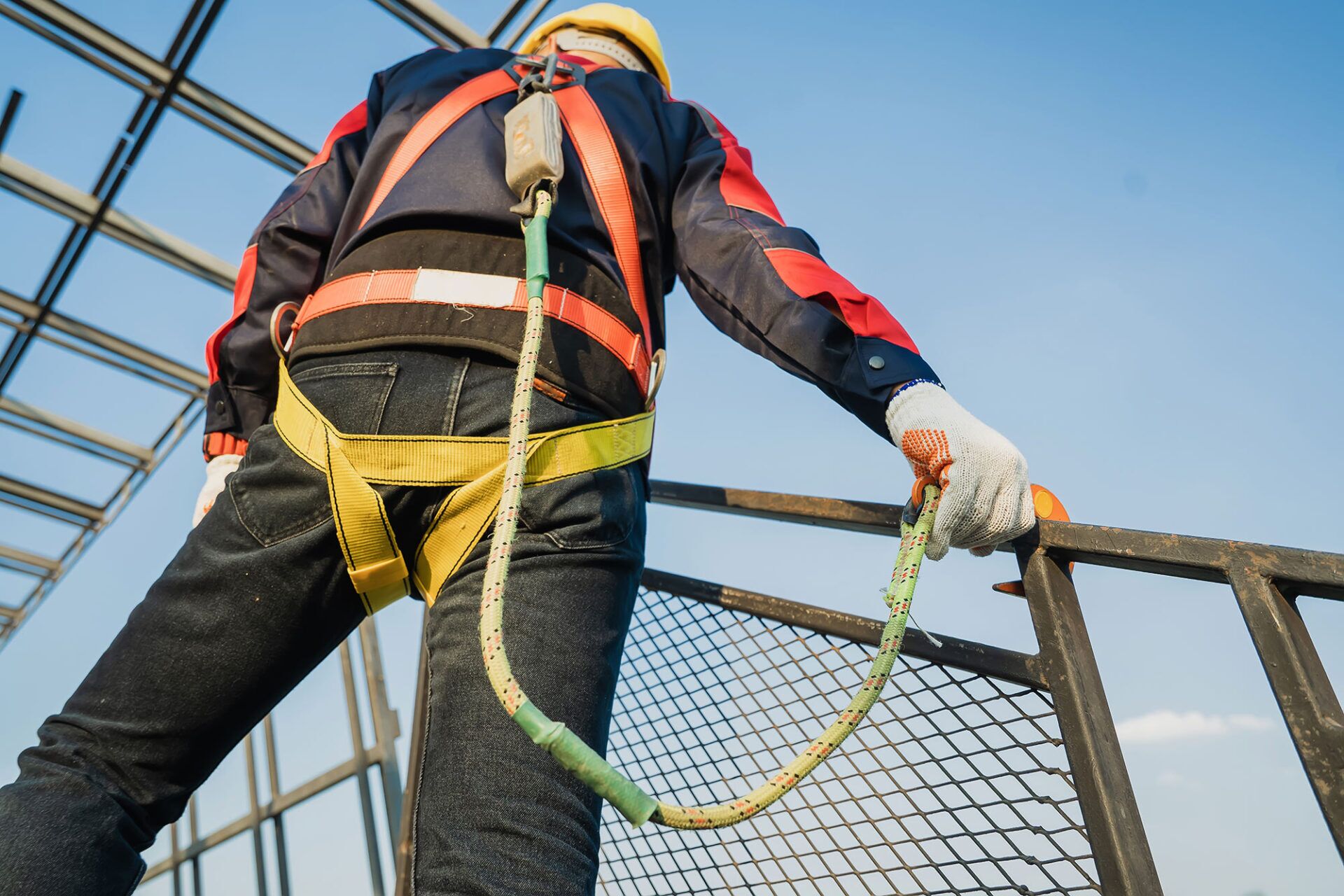 ** Worker wearing a safety harness and helmet, securely attached to a safety railing while working at heights, emphasizing the importance of safety measures and risk mitigation in workplace environments.