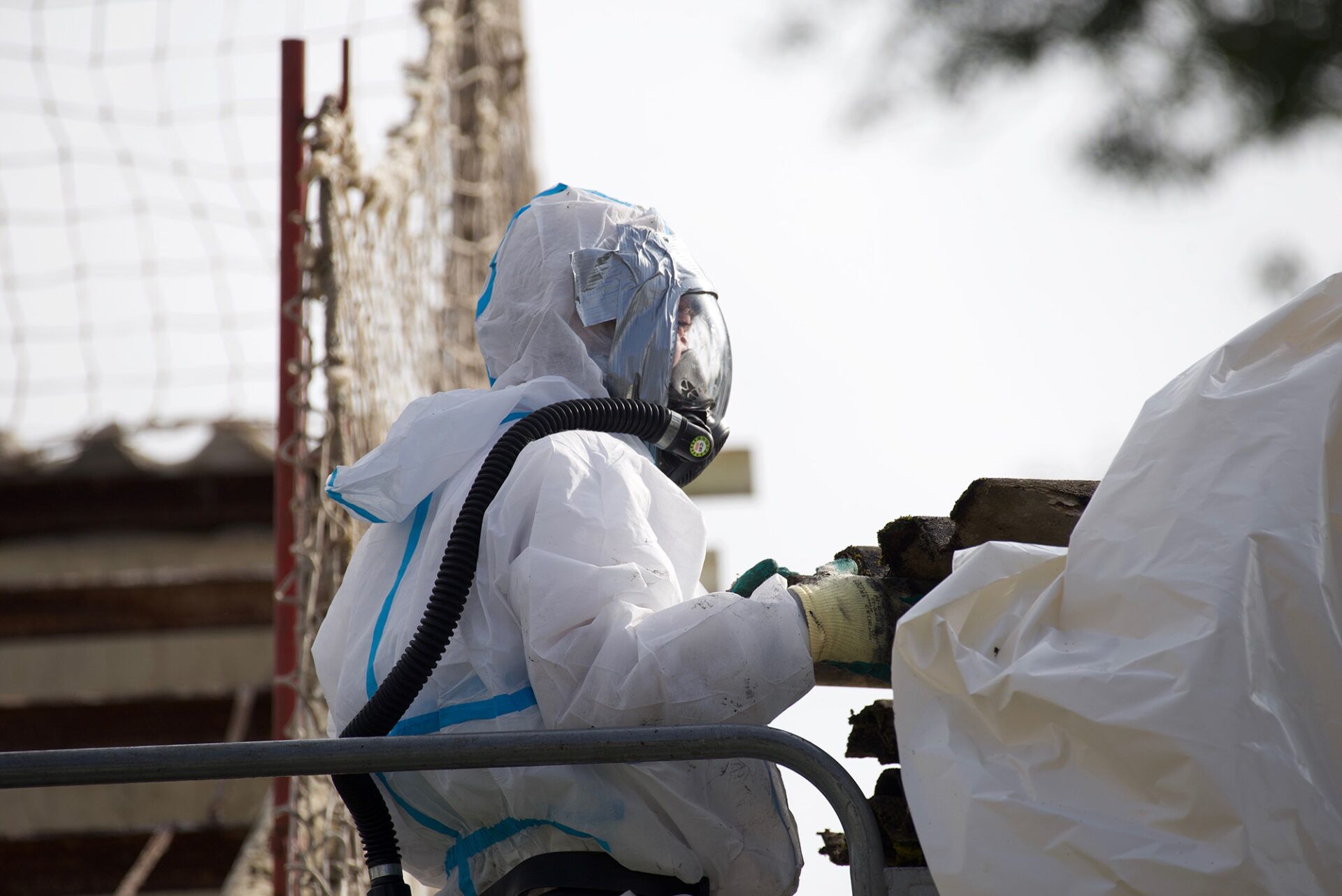 Worker in a protective suit and mask safely handling asbestos removal materials on a construction site, following the code of practice for asbestos safety.