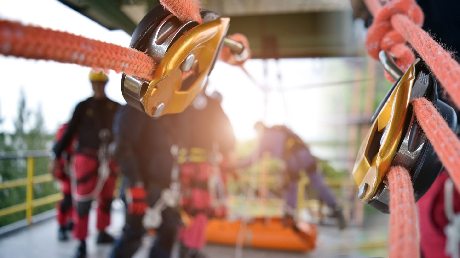 Close-up of safety equipment, including a pulley and safety ropes, with workers in harnesses in the background, emphasizing the importance of safety training for improving employee morale in the workplace.