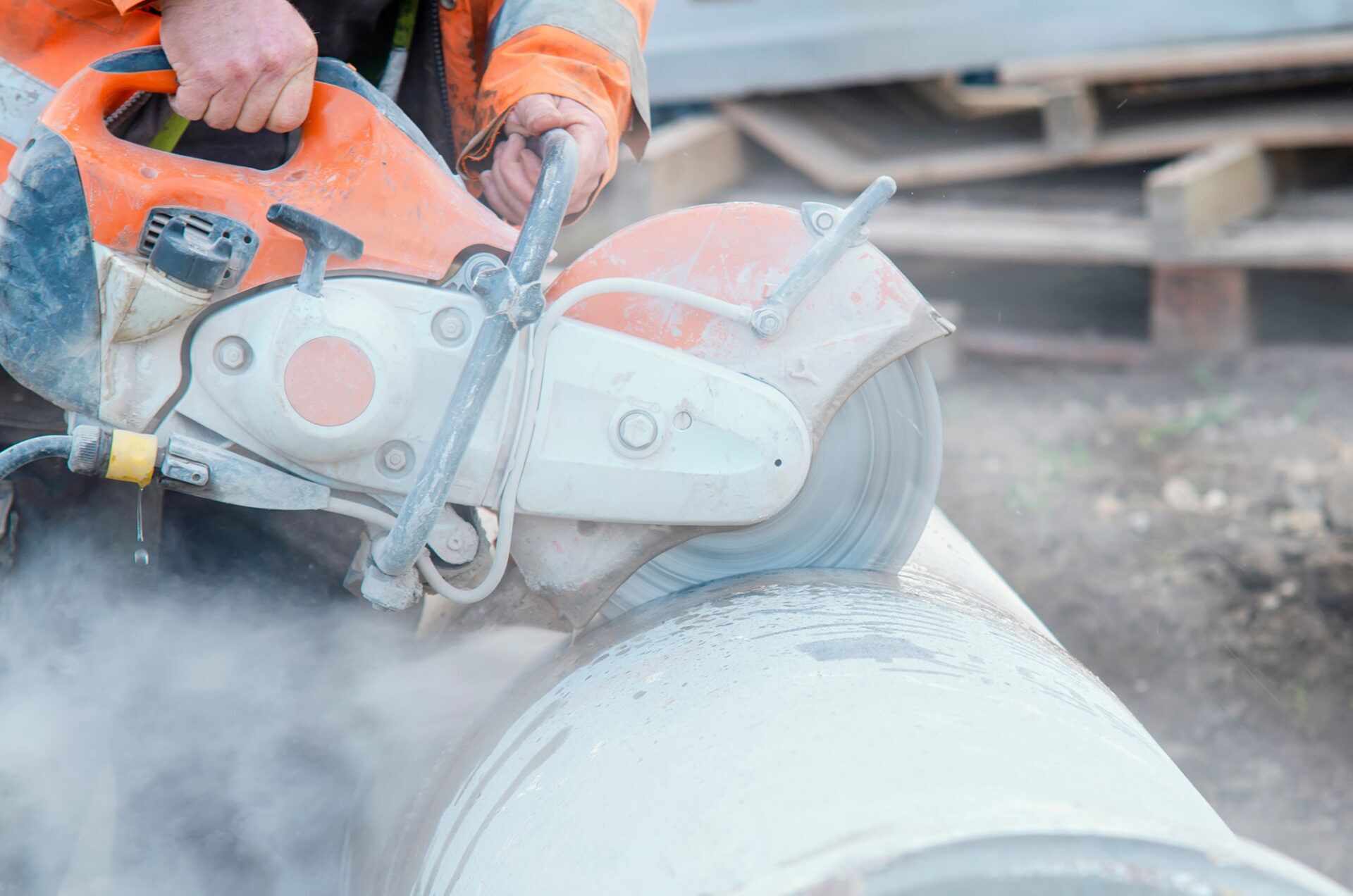 Construction worker using a concrete cutting saw on a pipe, illustrating silica exposure risks in the workplace.