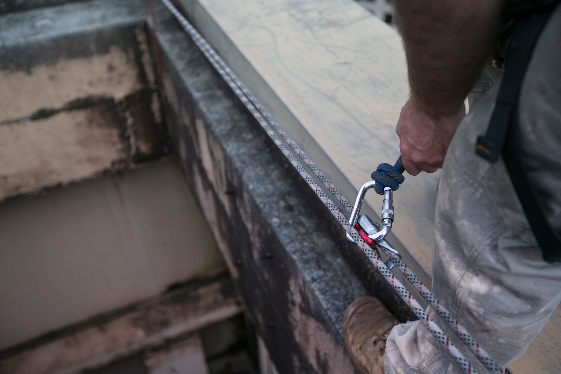 A person performing a safety inspection on an anchor point using a carabiner and rope, ensuring compliance with AS/NZS standards.