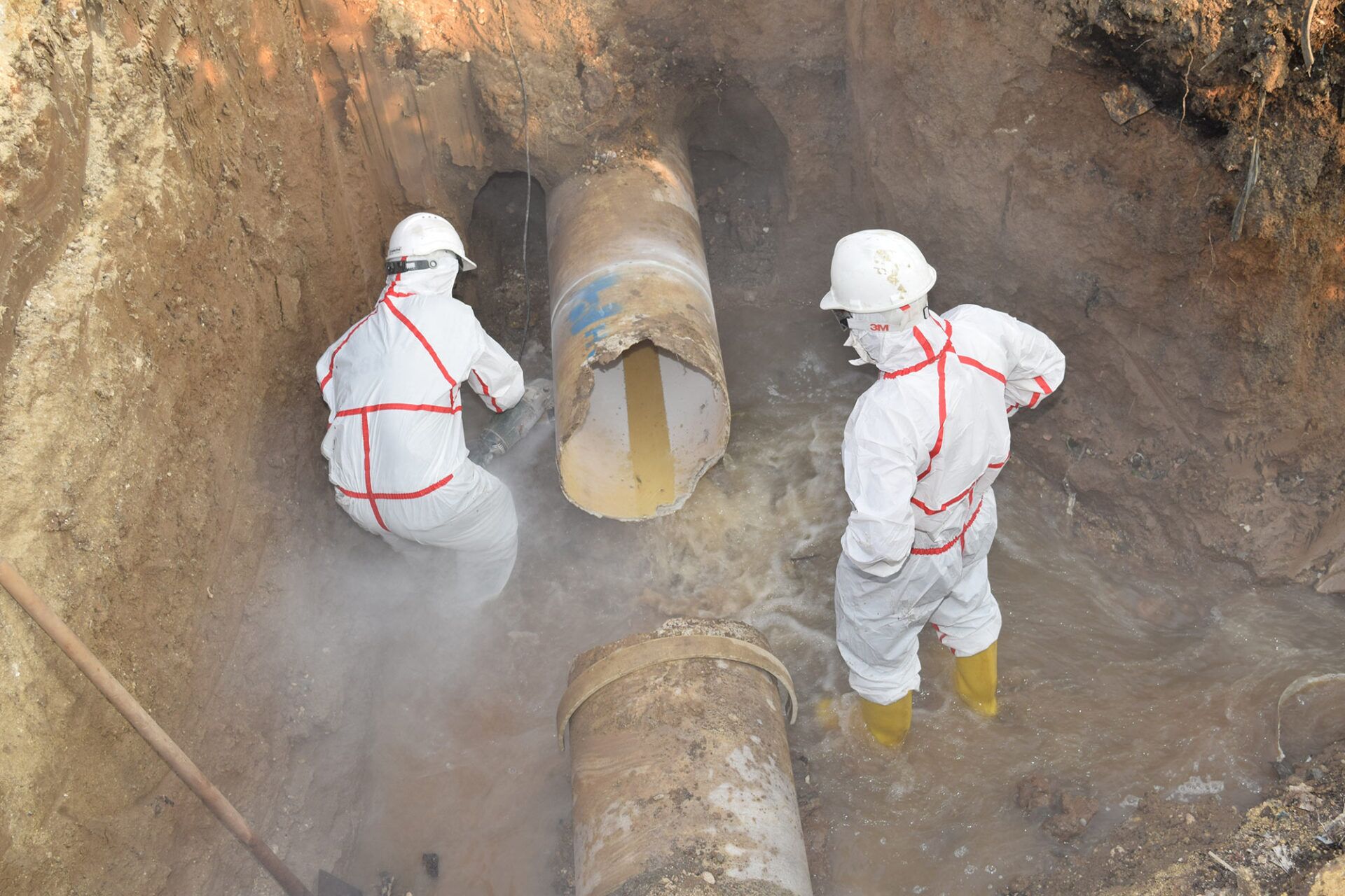 Two workers in protective gear conducting friable asbestos removal training in an excavation site, demonstrating safety protocols for handling hazardous materials.
