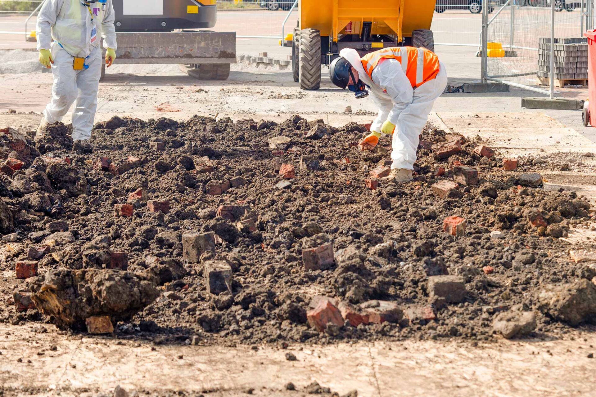 Workers in protective gear examining soil and debris on a construction site, highlighting safety procedures for asbestos awareness training.